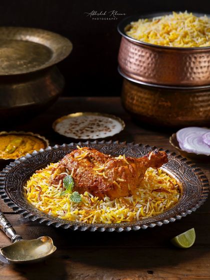 A wider angle of the Zafrani Chicken Dum Biryani, showing the full serving presentation with raita and salan, providing context for a menu.