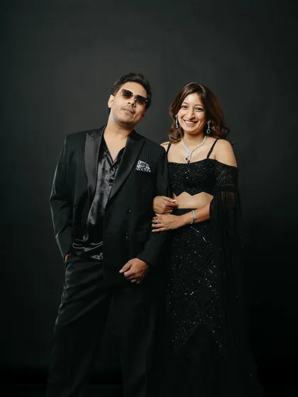 A classic and stylish couple portrait from a studio session. Dressed in coordinated black evening wear, they stand together exuding confidence and grace against a solid black backdrop, perfect for a timeless pre-wedding album.