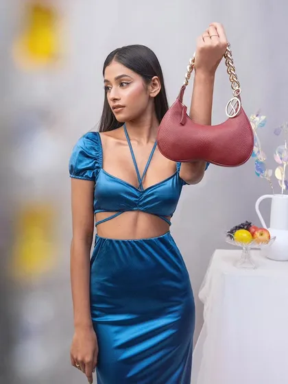 A full-length shot of a model holding a red Sarjaa handbag. This studio image focuses on the relationship between the accessory and the complete outfit, set against a soft, neutral background.