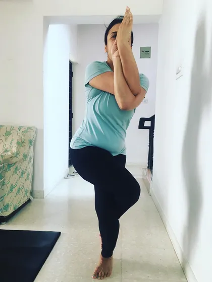 A front view of a student in Garudasana (Eagle Pose), showing the arm wrap that stretches the upper back and shoulders.