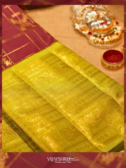 A close-up of the rich lime green zari border against the checked wine-colored body.