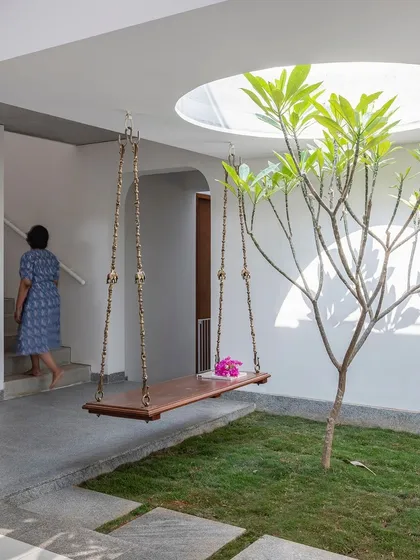 A resident enjoys the central courtyard, a tranquil space designed for pause and reflection. The use of natural grass, a Frangipani tree, and a traditional Indian swing creates a serene atmosphere.