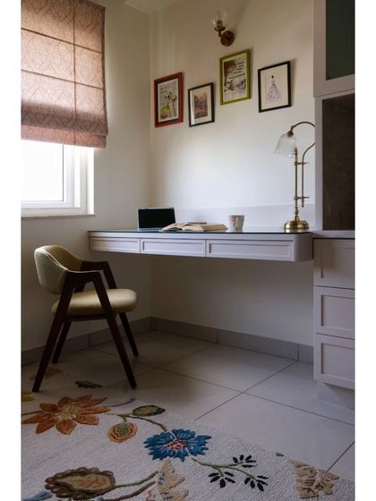 A cozy reading and working nook created in the home. The desk is finished in a soft white, contrasted by an olive-green chair, and the space is anchored by a stunning floral hand-tufted rug.