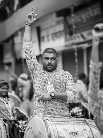 A powerful black and white portrait of a dhol player giving a signal, his arm raised high.