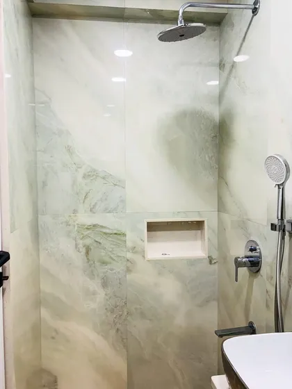 A view of the walk-in shower area with light green marble-finish tiles and a built-in niche for toiletries.