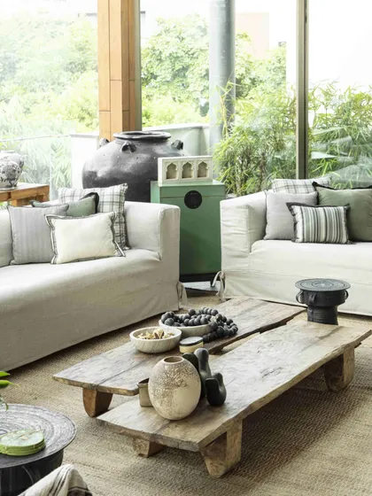 The conservatory at the Bammi Residence, designed with a Wabi-Sabi ethos. The space features a rustic coffee table from Nagaland, comfortable sofas, and large glass walls that blur the line between indoors and outdoors.