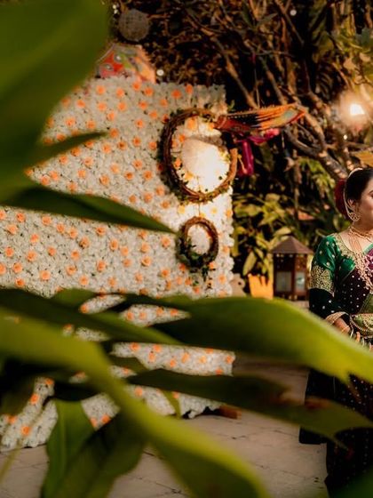 A candid portrait of a bride in her green nauvari saree, framed by lush green leaves. The soft lighting and natural setting give this image a calm and serene feel.