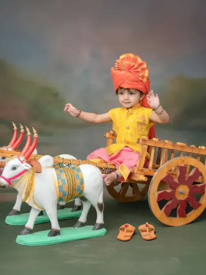 This photoshoot captures the simple charm of Maharashtrian rural life. Your child can pose on a decorated miniature bullock cart, wearing a colorful kurta and pheta for a truly desi feel.