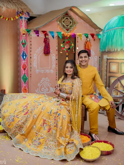 A couple poses against a vibrant, village-themed backdrop for their traditional Haldi ceremony.