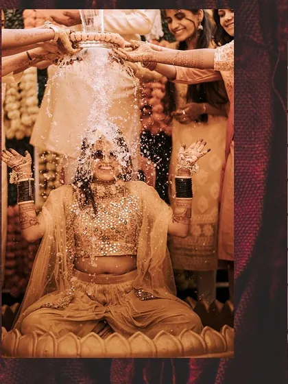 A joyful shot of the bride with her hands up, being showered with water during her fun-filled Haldi.