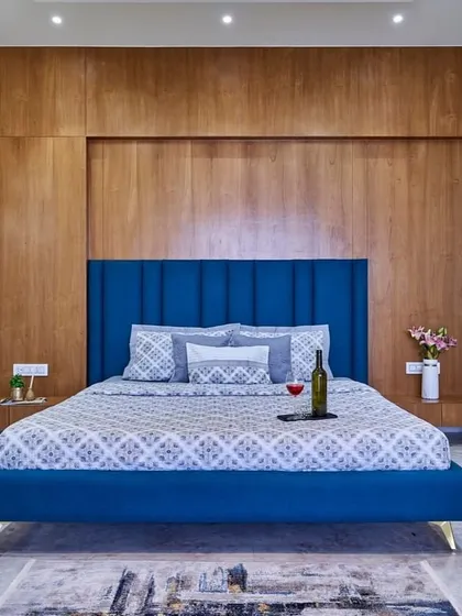 A bold and beautiful bedroom design. The royal blue upholstered bed stands out against the warm wood-paneled wall, creating a look that is both modern and timeless. The minimalist wall sconce adds an artistic touch.