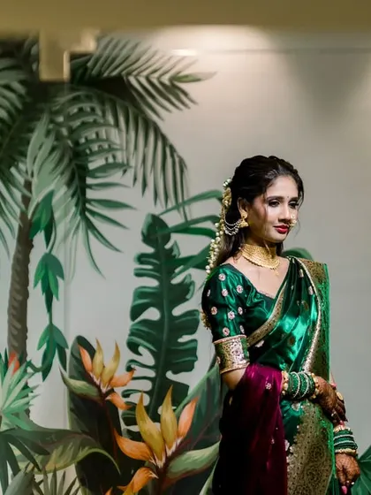 A beautiful portrait of a Marathi bride against a tropical-themed wall. Her emerald green saree complements the background perfectly, creating a stylish and cohesive image.