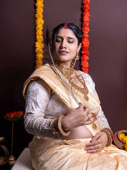 A serene and traditional maternity portrait. The mom-to-be, dressed in a beautiful saree, holds a peacock feather, adding a symbolic and cultural element.