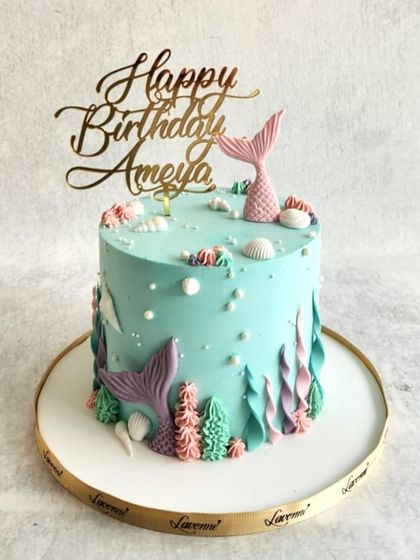 A mermaid-themed cake for Ameya's birthday. The design features different shades of buttercream to create an underwater effect, with cute mermaid tails and seashells.