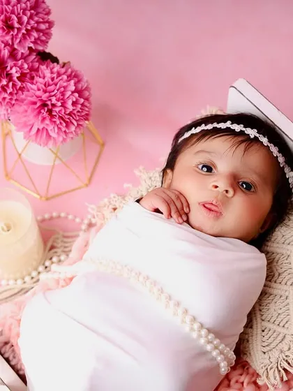 An overhead view of the awake baby in the miniature bed, showing the full composition with the pink background and macrame details.