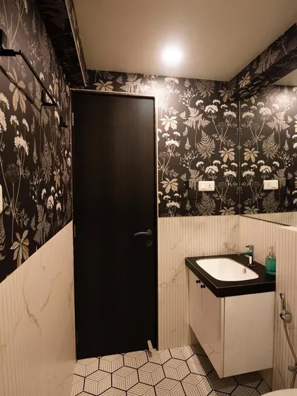 A bathroom revamp featuring bold floral wallpaper on the upper half of the wall and simple white tiles below. The hexagonal floor tiles add another layer of pattern, creating a dramatic and stylish powder room.