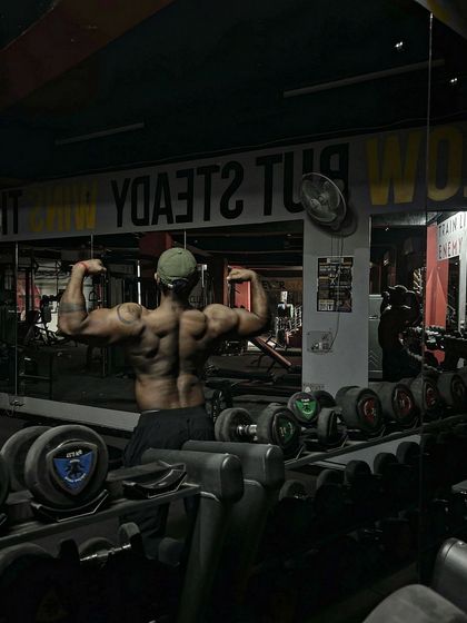 A back double bicep pose in the same moody lighting. The shadows highlight the depth and detail of the back.