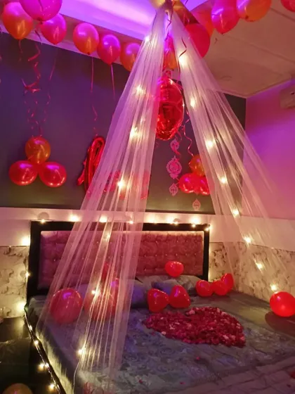 A different angle of a romantic canopy decoration, with purple mood lighting enhancing the dreamy atmosphere. The balloons floating on the ceiling add to the celebratory feel.