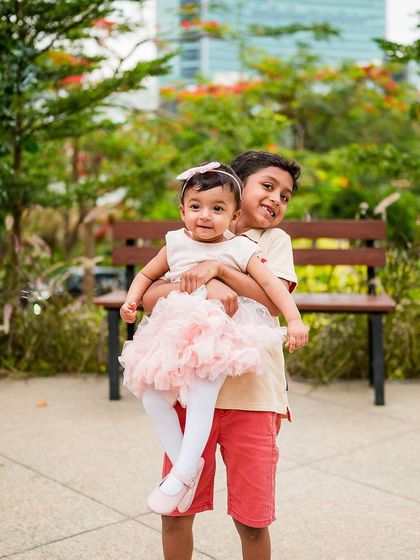 A sweet photo of an older brother holding his baby sister in a garden setting. Capturing sibling love is a joy.