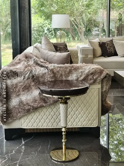 A detail from the Vasant Kunj glass house, showing a quilted leather sofa draped with a faux fur throw and a bespoke side table. This image captures the cozy, tactile elements we incorporate to make a space feel like home.