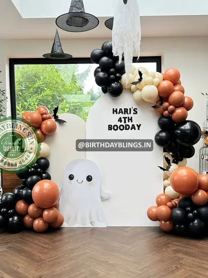 A spooky and fun "Booday" party for a 4th birthday. This Halloween-themed setup includes a cute ghost cutout, witch hats, and a black and orange balloon arch.