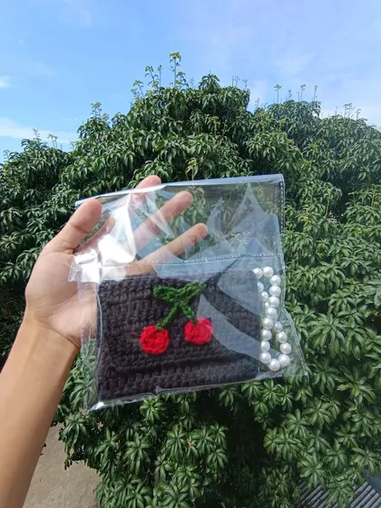 A black pocket purse with a cherry design and pearl strap, neatly packaged for a client's college fest.