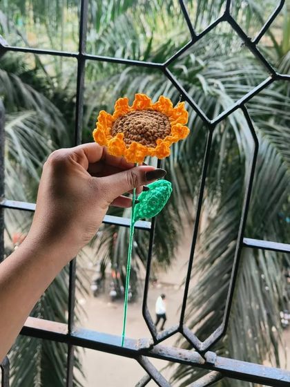 A single crochet sunflower held up against the window. The natural light really shows off the bright yellow yarn and the handmade details.