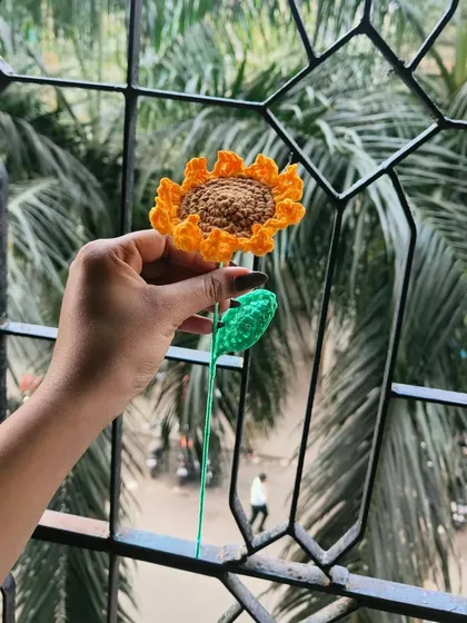 My handmade crochet sunflower held up against the sky. I love how the light catches the texture of the yellow petals and the brown center.