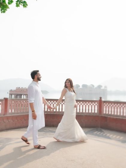 A beautiful pre-wedding photograph taken at Jal Mahal in Jaipur. The couple, dressed in elegant white attire, walks hand-in-hand, creating a timeless and romantic destination wedding memory.