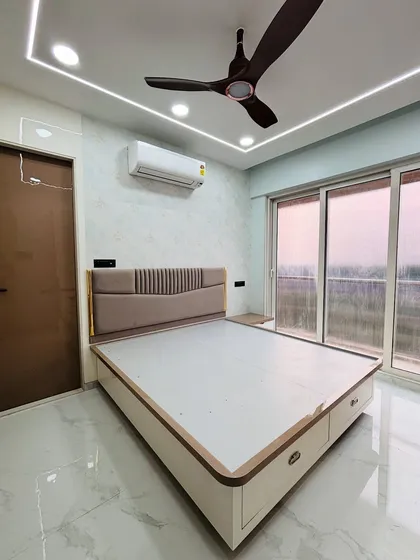 A beautifully finished bedroom with a custom upholstered headboard and a bed with built-in drawers for extra storage. The false ceiling with cove lighting adds a soft, relaxing glow.