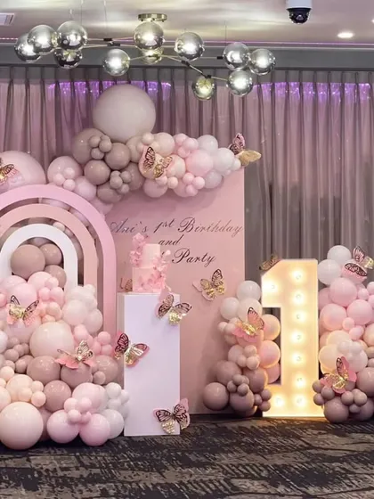 A beautiful butterfly-themed first birthday in shades of dusty pink and rose gold. The decor includes a large light-up number "1" and intricate balloon work with butterfly accents.