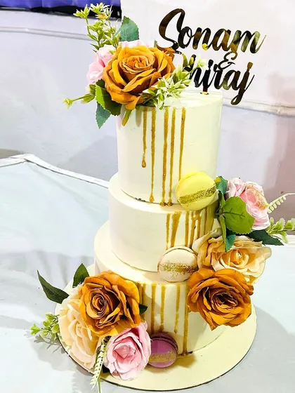 A three-tiered custom wedding cake designed to be the centerpiece of a special day. This elegant cake features a delicate golden drip, macarons, and a cascade of beautiful flowers to match the wedding's theme.