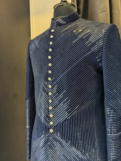 A close-up of a navy blue Indo-Western jacket with intricate, patterned embroidery and a full button-down front. This piece is perfect for a formal yet stylish reception look.