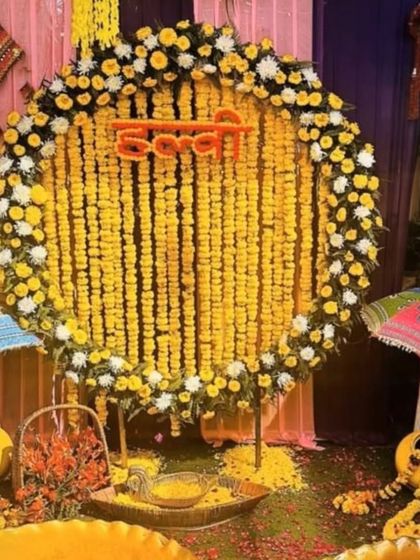 A festive Haldi setup with a circular marigold backdrop and traditional Rajasthani umbrellas. The "Haldi" sign in Hindi adds an authentic touch to this colorful arrangement.