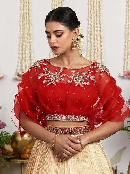 A detailed shot of the red organza cape blouse, showing the intricate embroidery and the scalloped hem.