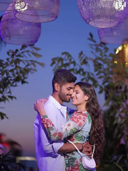 A romantic evening portrait of a couple embracing under purple lanterns, with the twilight sky creating a magical atmosphere.