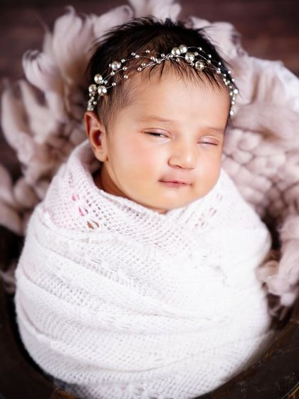 A precious newborn wearing a pearl headband, swaddled in white and sleeping soundly. A simple and elegant portrait.