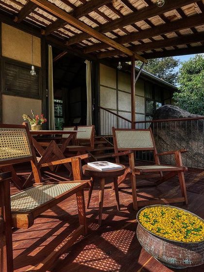 The wooden deck of the prefab cottage is an essential living space, furnished with classic planters' chairs for enjoying the view and the tropical climate.