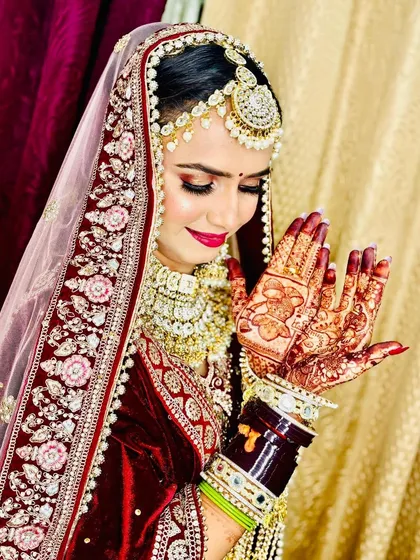 A shy, smiling bride with her hands in a prayer pose, showing off the beautiful color of her mehndi.