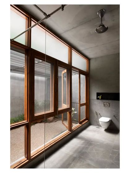 This bathroom in the 'House of Canopies' opens to a private gravel court, blending the rawness of the polished concrete interior with the natural elements outside. The large wooden window frames add warmth to the composition.
