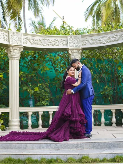 A full-length shot of the couple in a garden gazebo. The bride's long, ruffled purple gown is the star of this elegant pre-wedding photo.