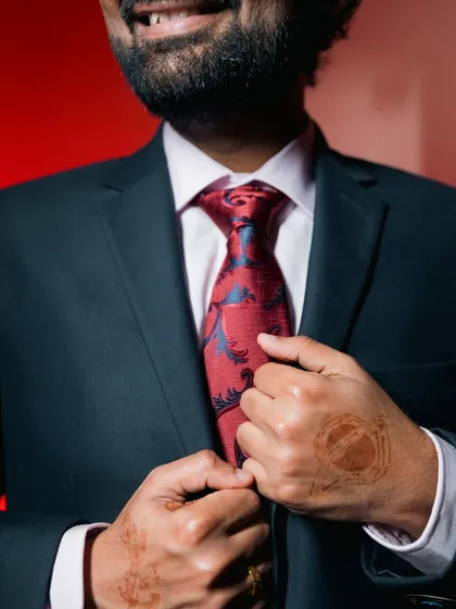 A close-up on the groom's patterned tie and henna-adorned hand.