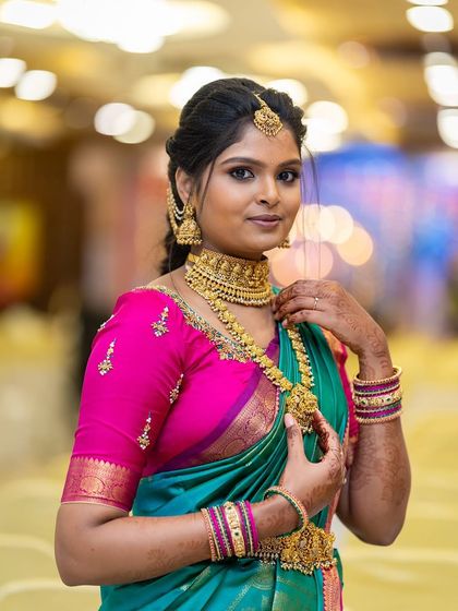A stunning portrait of our client Asha. She chose a classic gold-finish temple jewellery set, featuring a wide choker and a matching haram, which stands out beautifully against her vibrant teal and pink saree.