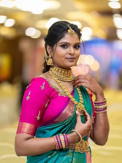 A stunning portrait of our client Asha. She chose a classic gold-finish temple jewellery set, featuring a wide choker and a matching haram, which stands out beautifully against her vibrant teal and pink saree.
