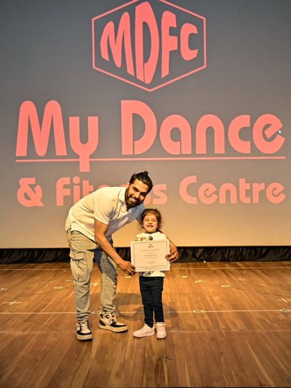 Another proud moment with Dea and her certificate, celebrating her achievement under the bright lights of the stage.