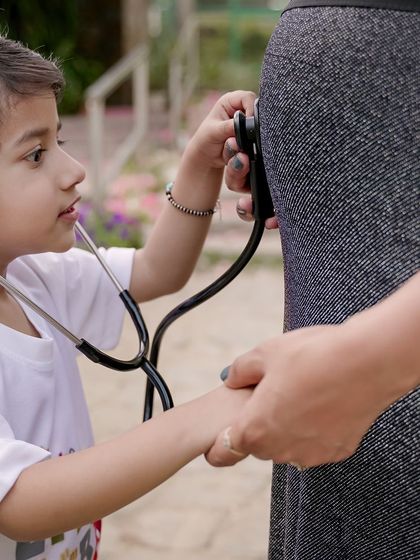 A playful and heartwarming shot of a big brother using a stethoscope on his mother's pregnant belly. Including siblings in maternity photos is a wonderful way to capture the family's journey.