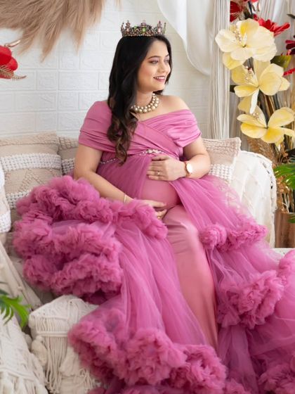 A luxurious portrait in a multi-layered pink gown. The expecting mother looks off to the side, creating a candid and elegant feel amidst the floral and boho decor of our studio.