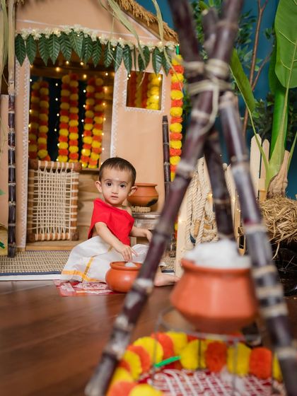 A baby sits by the traditional Pongal pot, looking curiously at the setup.