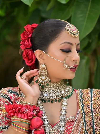 A close-up of a classic bridal look, featuring bold winged eyeliner, a deep red lip, and a beautiful floral bun with red roses. The kundan jewelry adds to the regal feel.