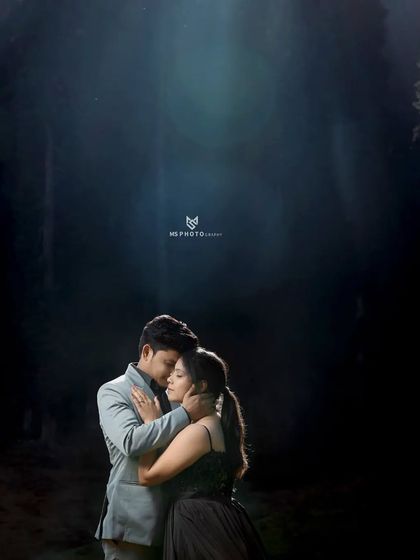 A dramatic and intimate embrace in a dark forest, with a single light source illuminating the couple. This creates a very moody and cinematic feel.